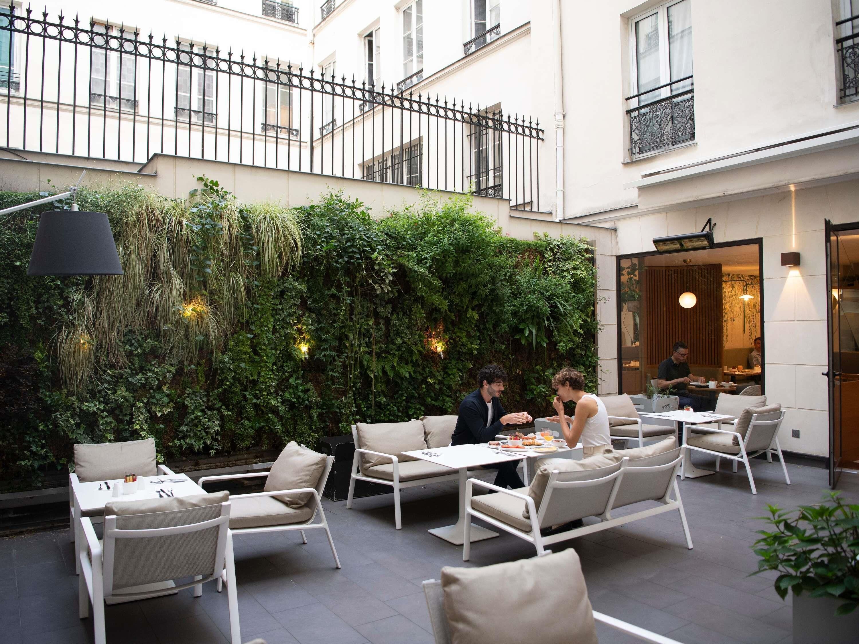 An outdoor seating area with white furniture and a lush green wall.