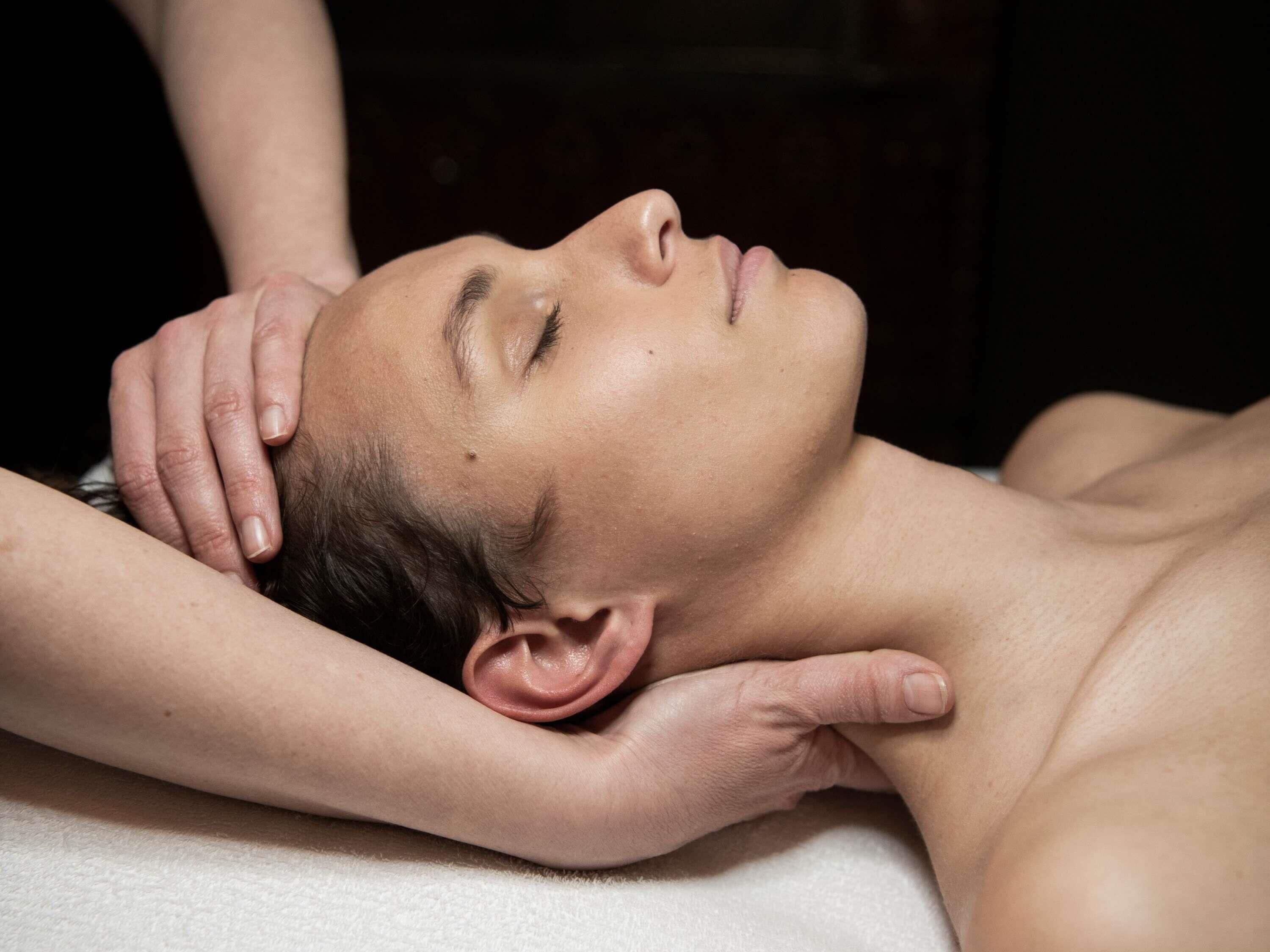 A person lying down with hands on their head and shoulders, suggesting a massage or relaxation setting.
