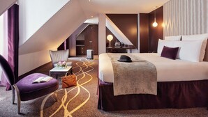 A modern hotel room with a bed, a desk, a chair, a small table, and a suitcase. - Mercure Paris Opéra Garnier (Paris)