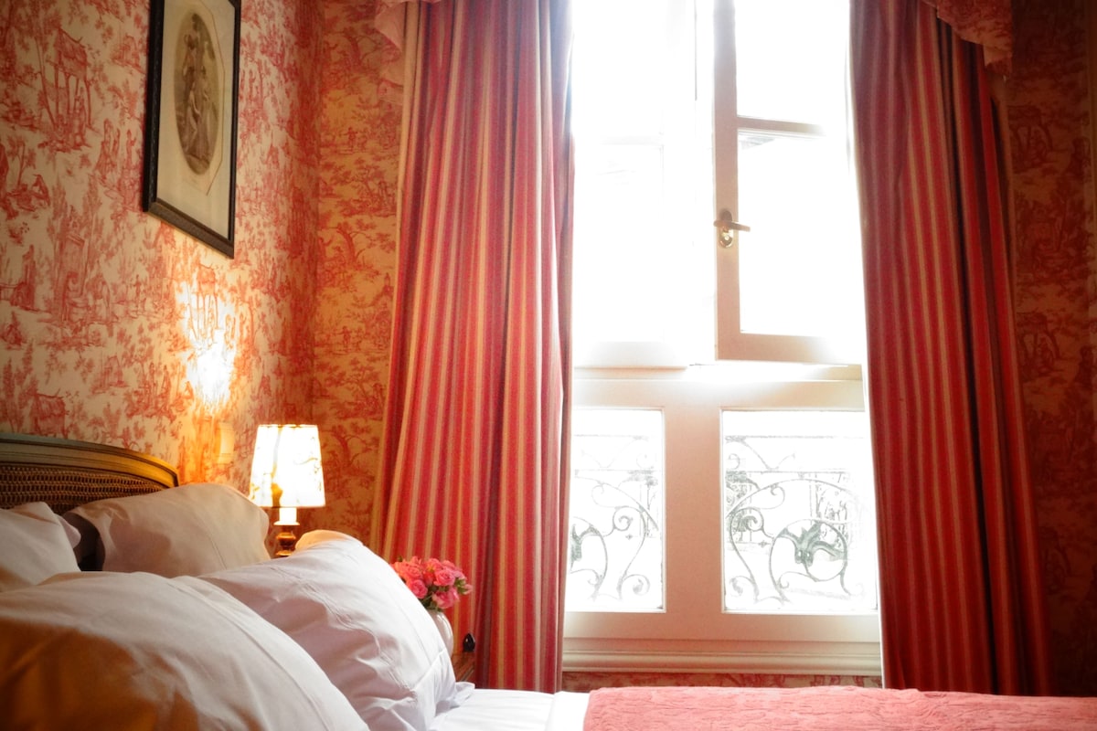 A hotel room with a bed, a nightstand, a lamp, and a window with curtains.