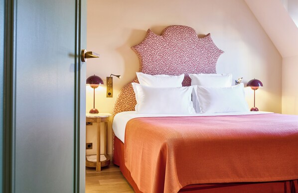 Una cama bien hecha con una colcha roja y almohadas blancas, un cabecero estampado de leopardo y dos lámparas de noche.