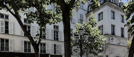 A tree-lined street with a building featuring white facades and shutters.