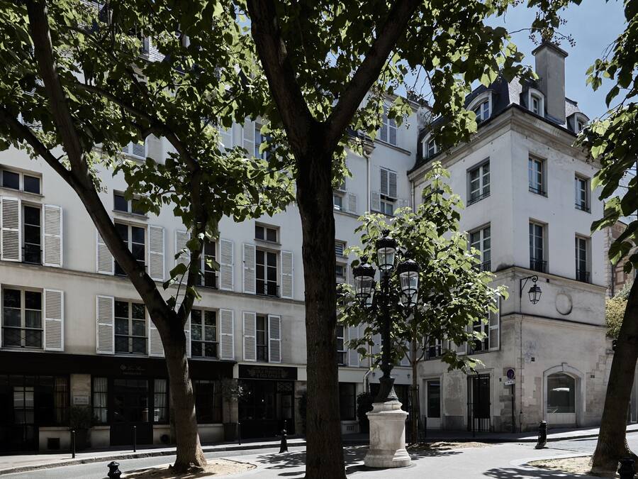 A tree-lined street with a building featuring white facades and shutters.