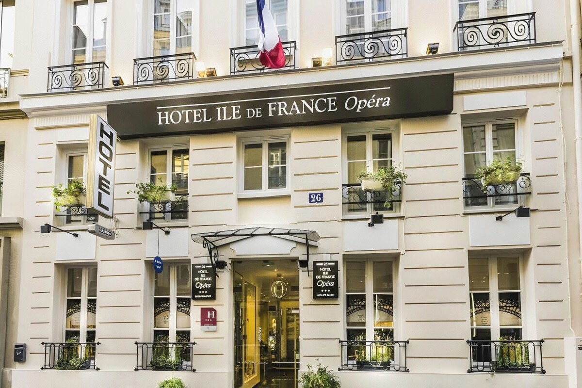 A hotel facade with balconies, a French flag, and signage for 'HOTEL ILE DE FRANCE Opéra.'