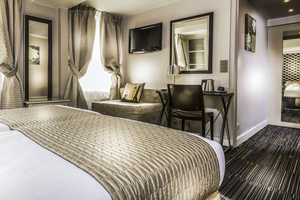 A hotel room with a large bed, a desk, a chair, a TV, and a mirror.