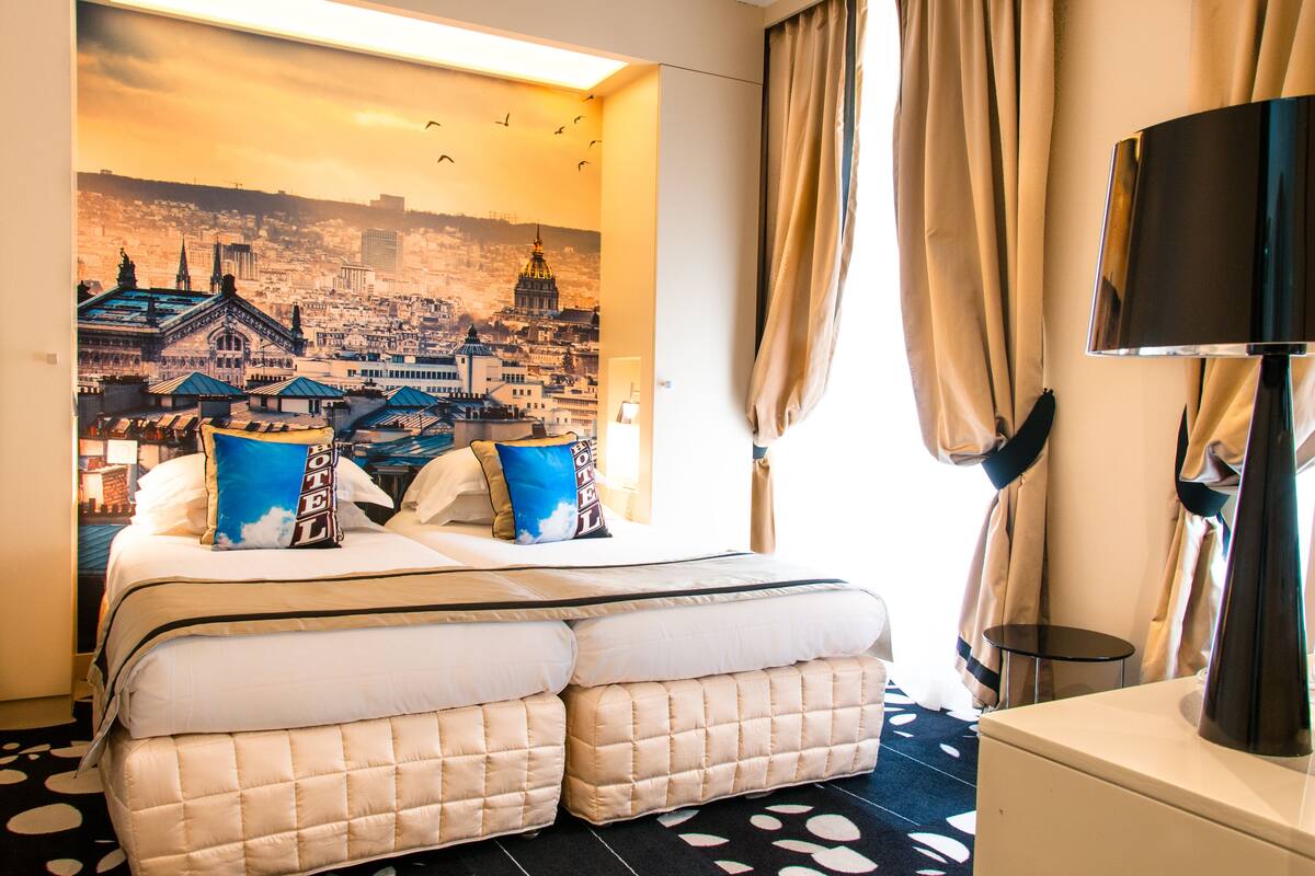 A hotel room with a large bed, a cityscape mural, a flat-screen TV, and a small bedside table.