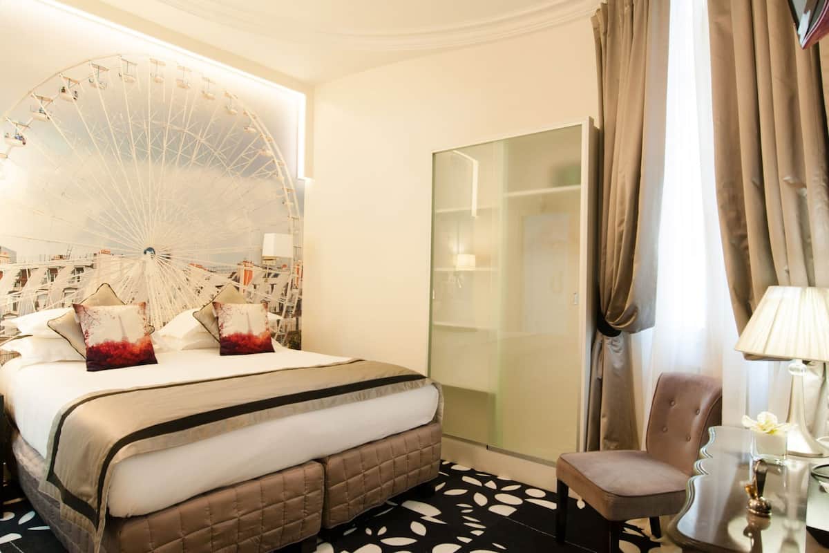 A hotel room with a bed, a chair, a lamp, and a large window with curtains.
