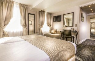A hotel room with a large bed, a desk with a chair, a TV, and a mirror.