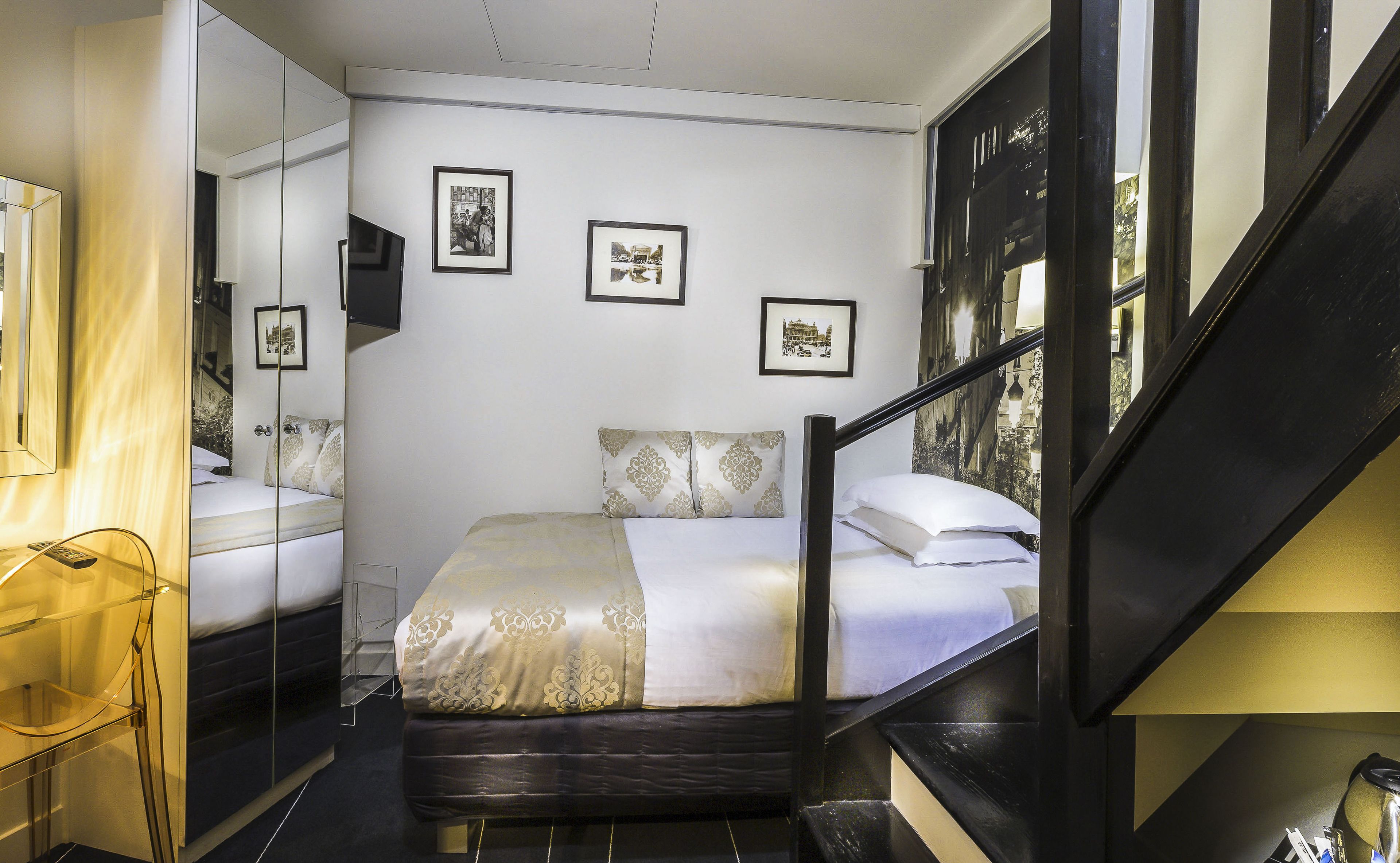 A hotel room with a bed, a mirror, a TV, and framed pictures on the wall.