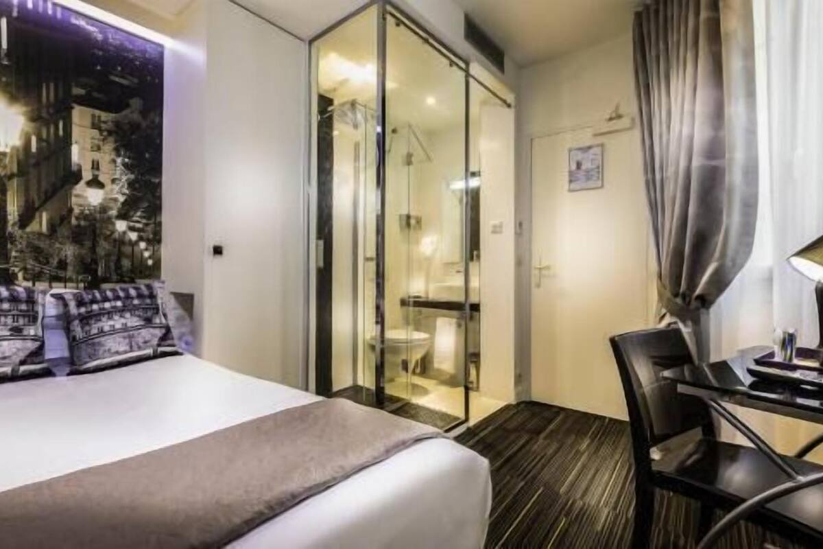 A hotel room with a bed, a desk, and a glass partition.