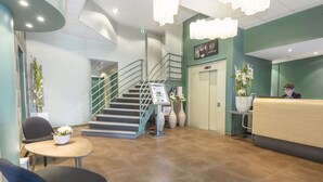 A reception area with a reception desk, a staircase, and a seating area with a table and chairs. - Hôtel Mercure Thionville Centre Porte du Luxembourg (Thionville)
