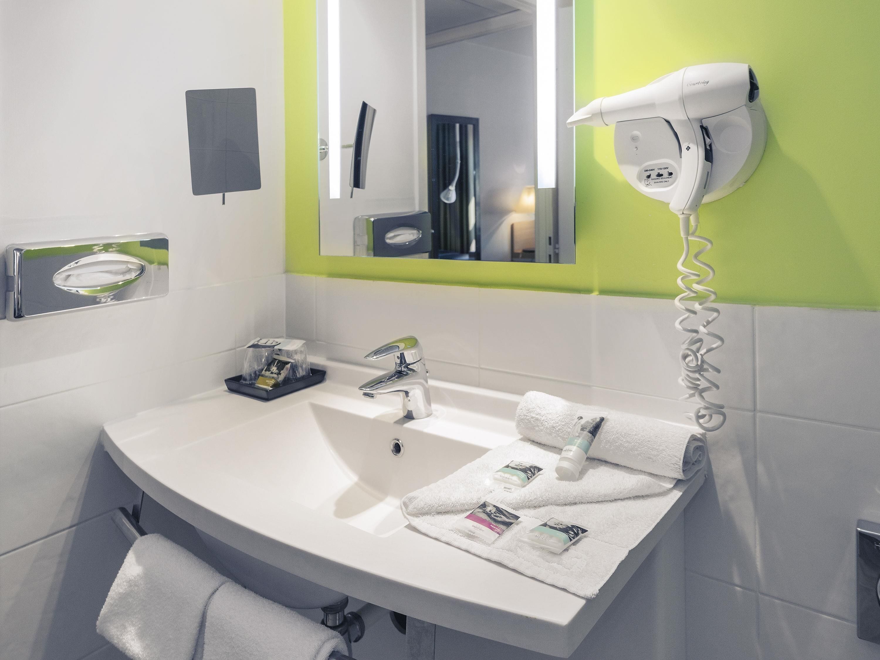 Un baño moderno con un lavamanos blanco, un espejo, un secador de pelo y un tendedero para toallas.