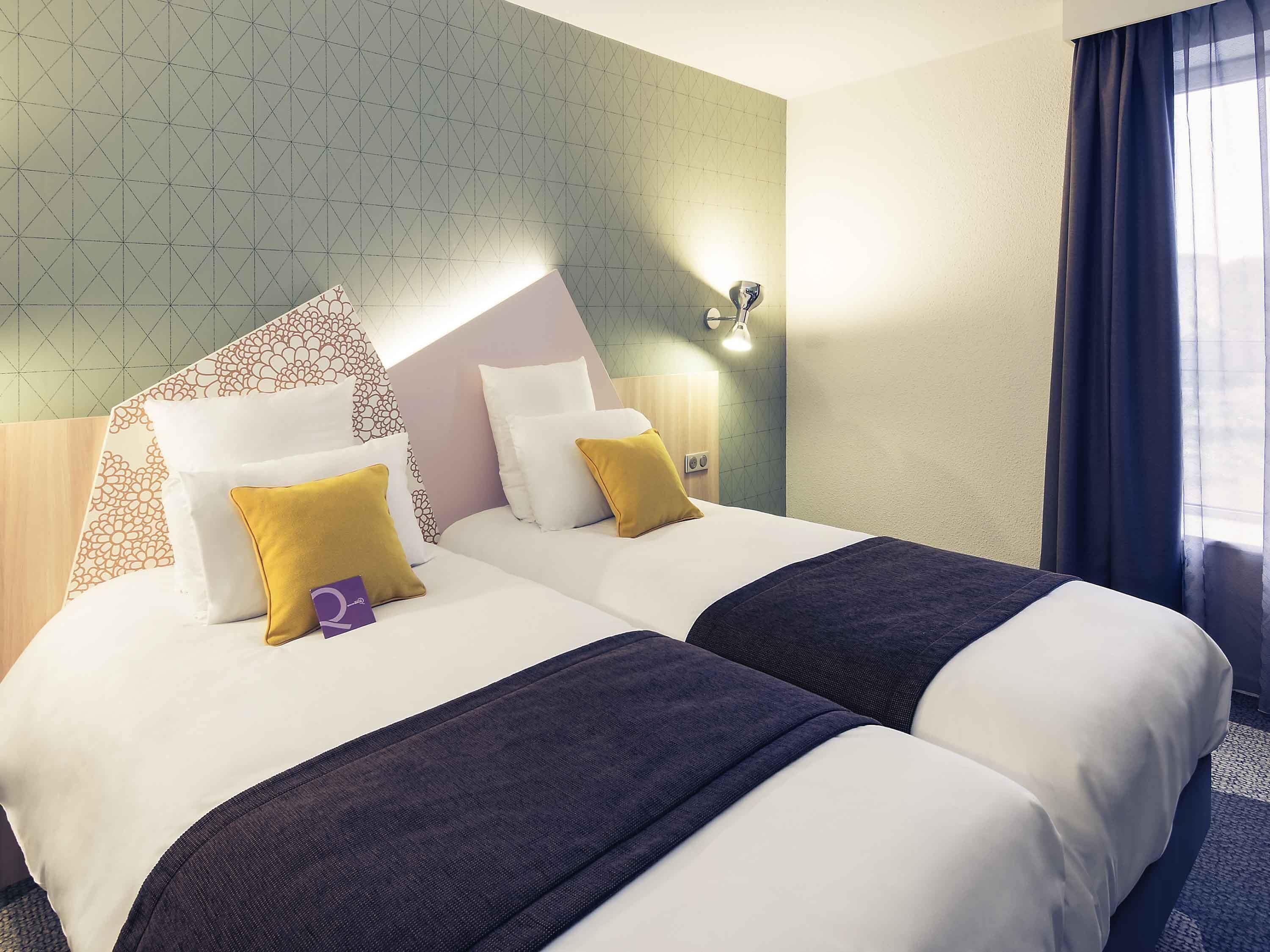 A hotel room with two beds, a patterned wall, a night light, and a window with curtains.