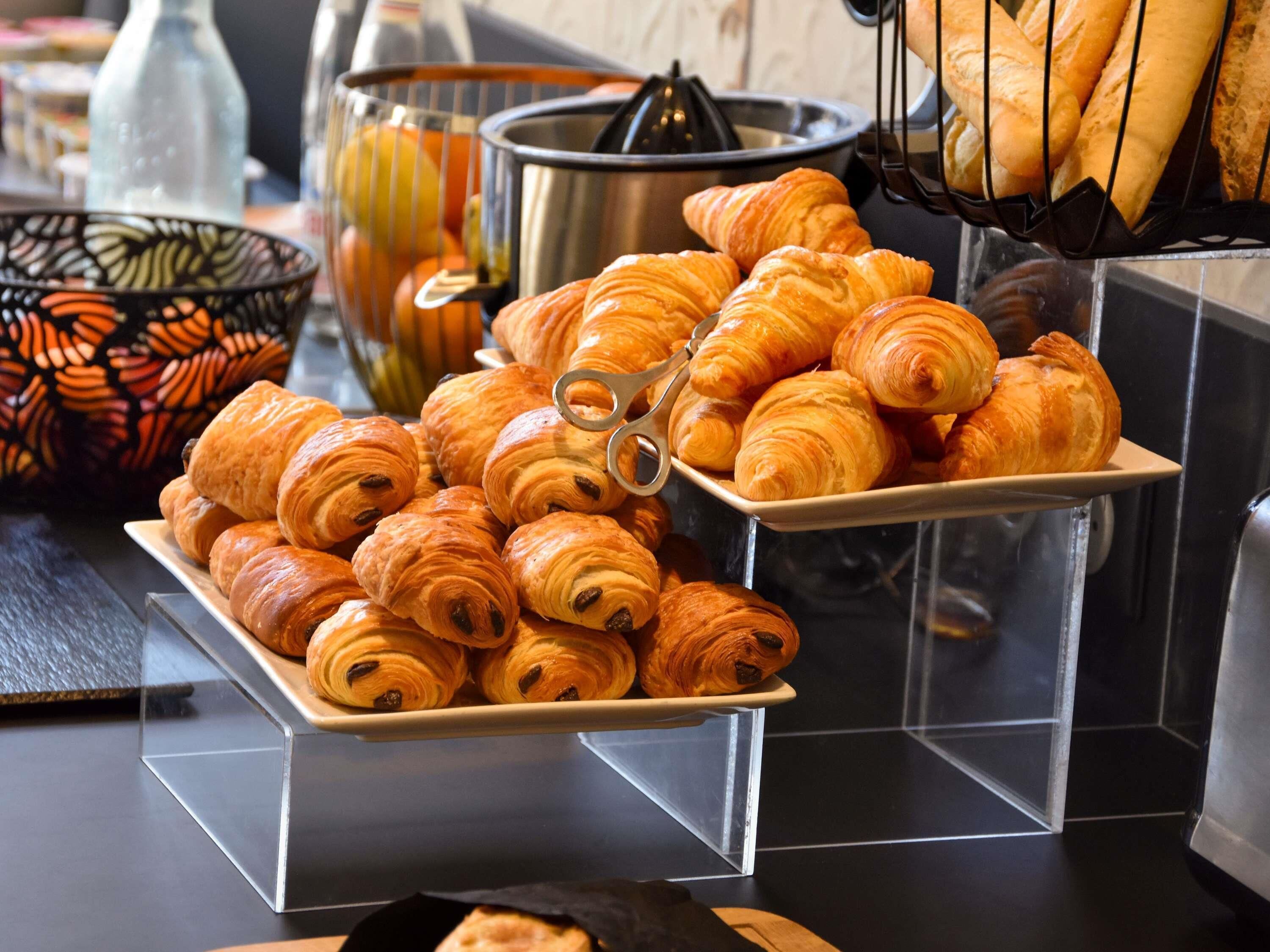A buffet table with croissants and a fruit juicer.