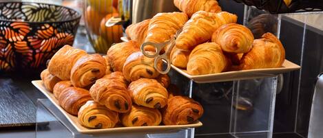 A buffet table with croissants and a fruit juicer.