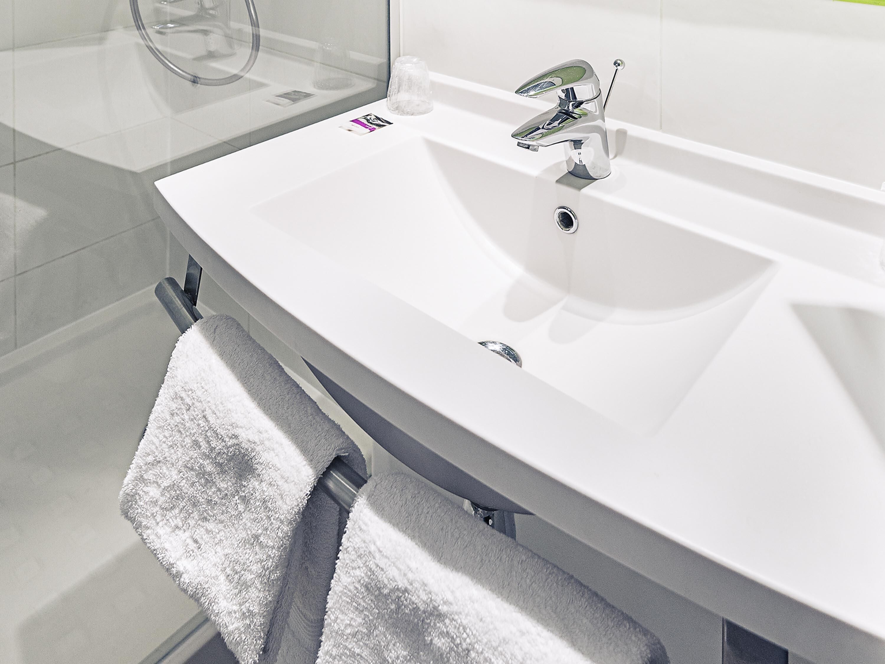 A bathroom with a white sink, a towel rack, and a glass shower enclosure.