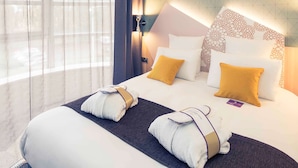 A hotel room with a large bed, two pillows, a headboard with a floral pattern, and a window with sheer curtains. - Hôtel Mercure Thionville Centre Porte du Luxembourg (Thionville)