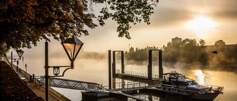A calm lake with a dock and a boat, surrounded by trees and a lamp post.