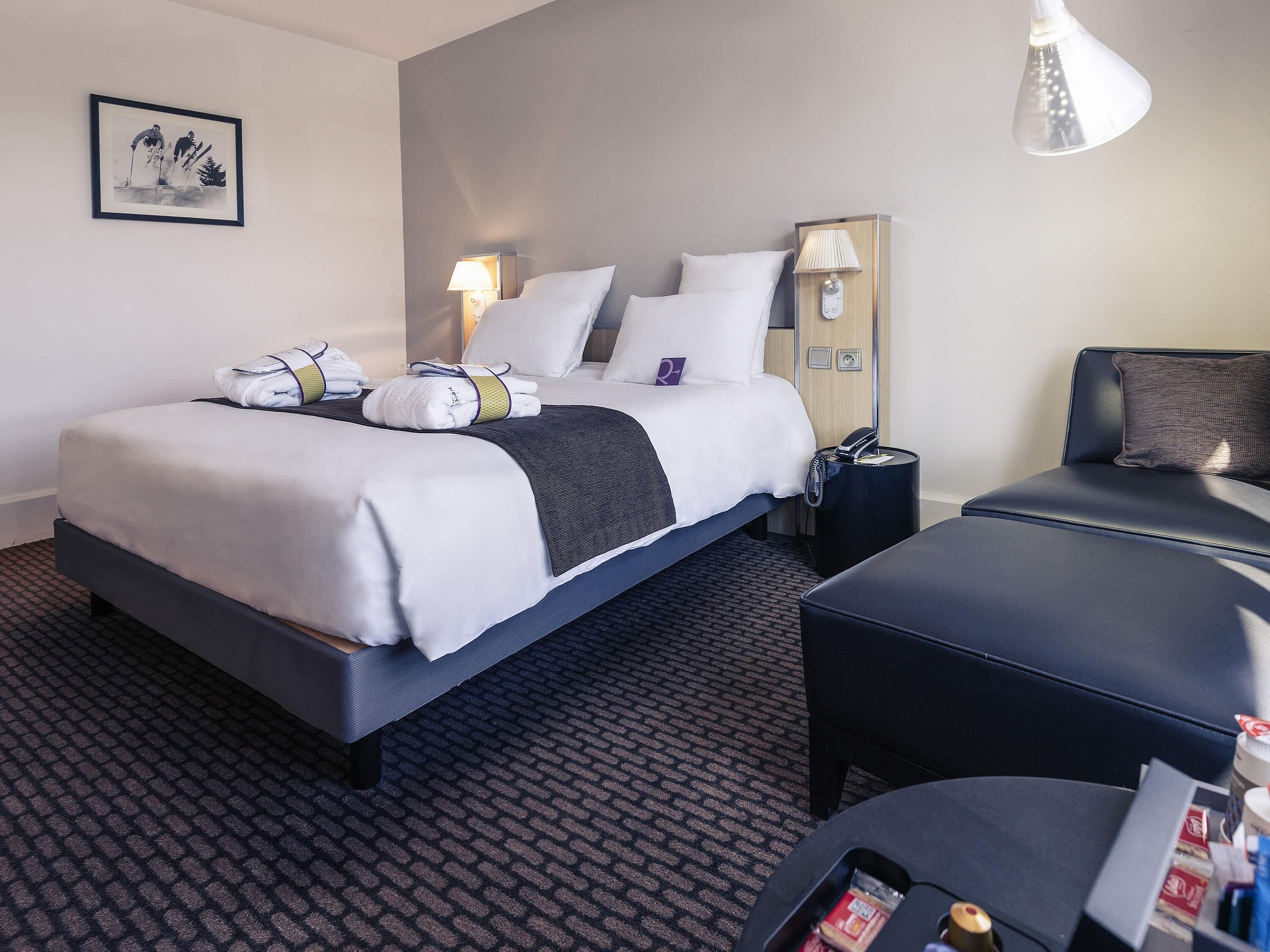 A hotel room with a bed, bedside table, lamp, and a small table with items on it.
