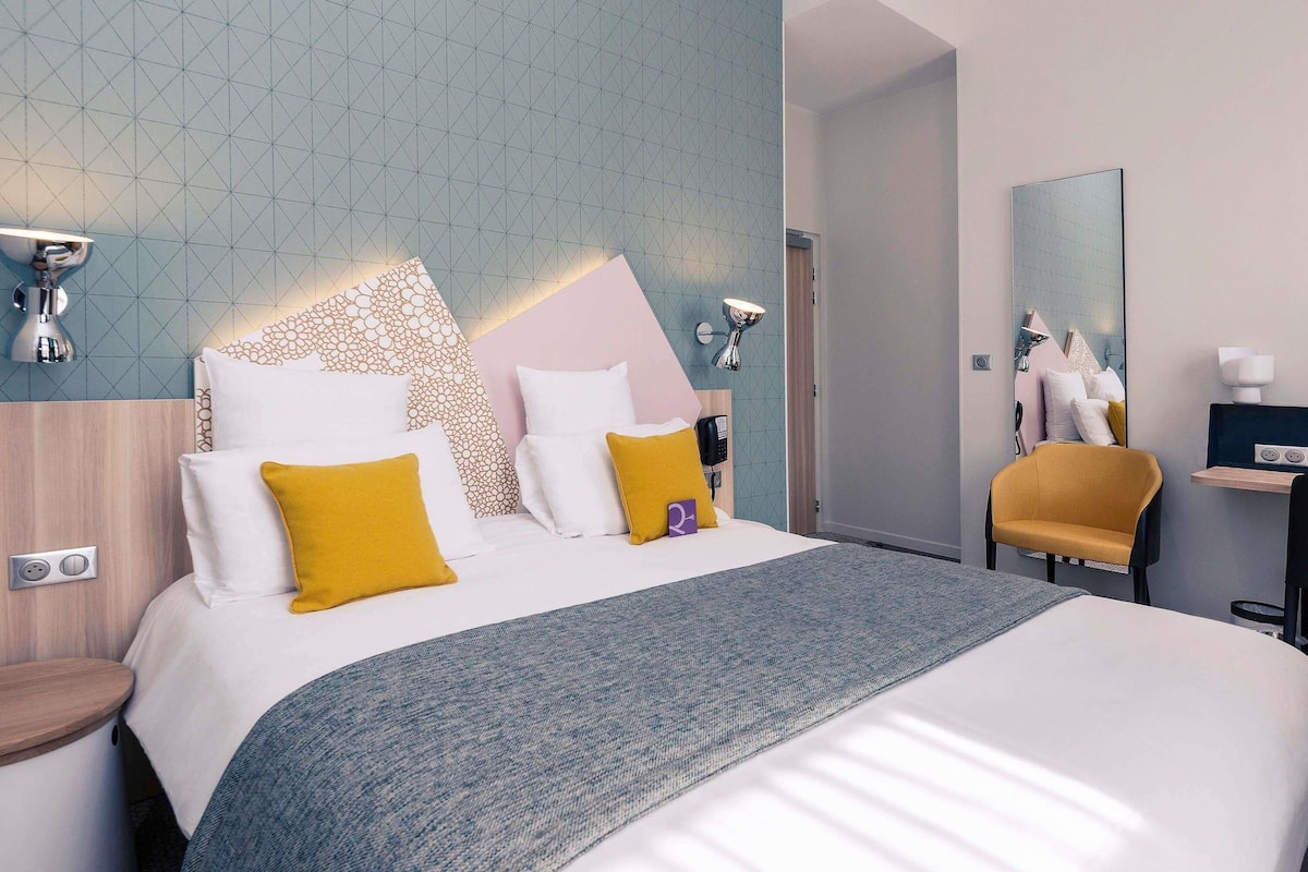 Une chambre d’hôtel moderne, équipée d’un lit, d’une table de chevet et d’une chaise.