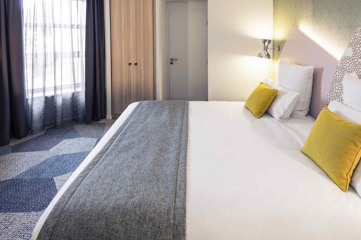 Une chambre d’hôtel avec un lit, une porte et une fenêtre avec des rideaux.