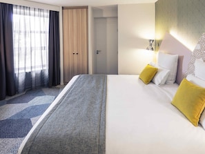 A hotel room with a bed, a door, and a window with curtains.
