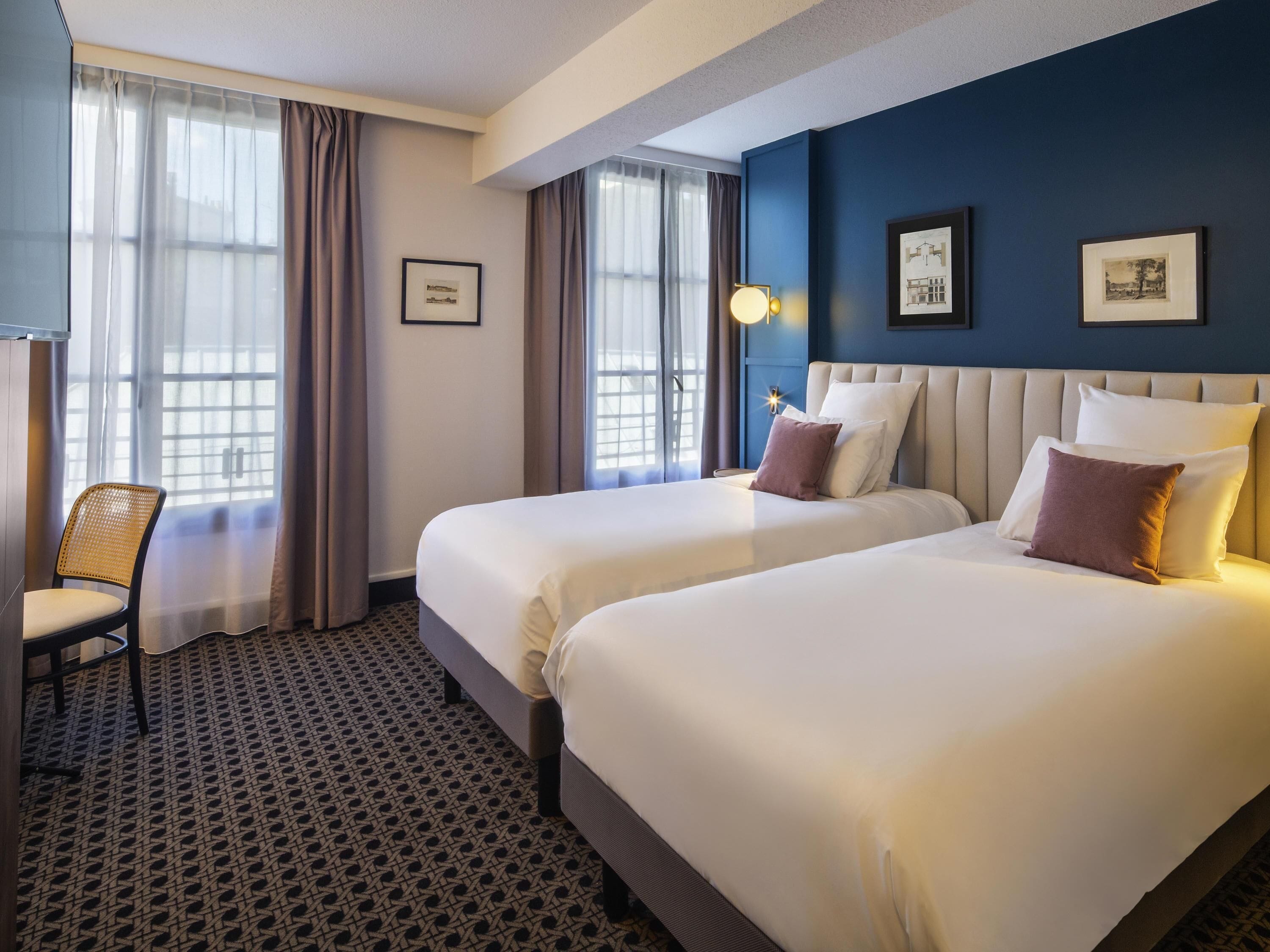 A hotel room with two beds, a chair, and a window with curtains.
