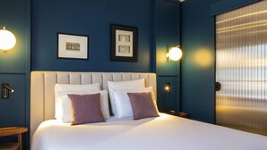 A hotel room with a large bed, two framed pictures on the wall, and two wall-mounted light fixtures. - Mercure Versailles Chateau (Versailles)