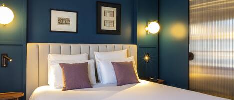 A hotel room with a large bed, two framed pictures on the wall, and two wall-mounted light fixtures.