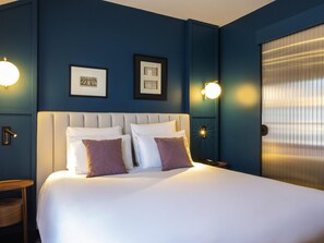 Una habitación de hotel con una cama grande, dos cuadros en la pared y dos lámparas fijadas a la pared.