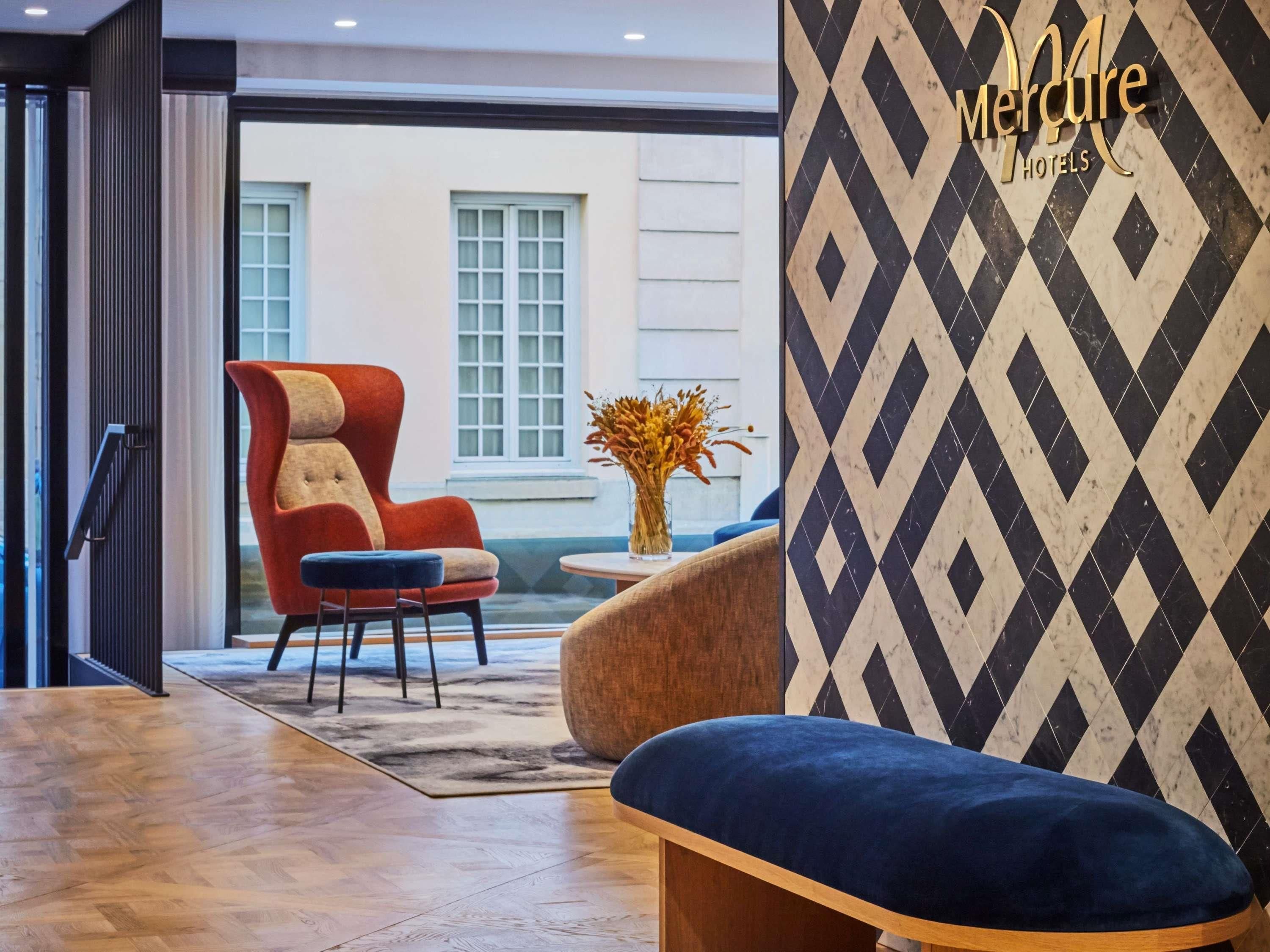 A modern hotel lobby with a red armchair, a blue sofa, and a patterned wall.