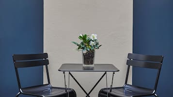 Un pequeño espacio al aire libre con dos sillas, una mesa, una planta en maceta y una lámpara fijada a la pared.