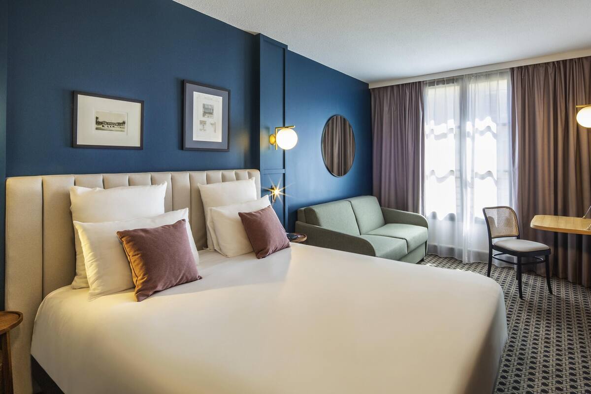 A hotel room with a large bed, a sofa, a dining table, and two framed pictures on the wall.