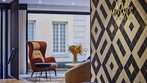 A modern hotel lobby with a red armchair, a blue sofa, and a patterned wall. - Mercure Versailles Chateau (Versailles)
