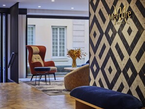 Un hall de hotel con un sillón moderno, una mesa redonda con un florero y una pared con diseño.