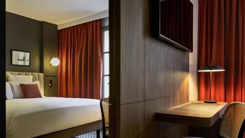 A hotel room with a bed, a desk, a chair, a lamp, and a mirror.