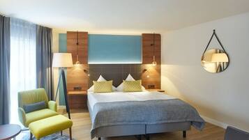 A modern hotel room with a bed, bedside tables, a chair, a lamp, and a mirror.