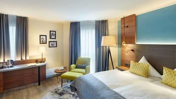 Habitación de hotel con cama, escritorio, silla, lámpara y una pequeña mesa.