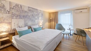 A hotel room with a large bed, a desk with a chair, a small table with a chair, and a large window with curtains. - Aquis Grana City Hotel (Aachen)