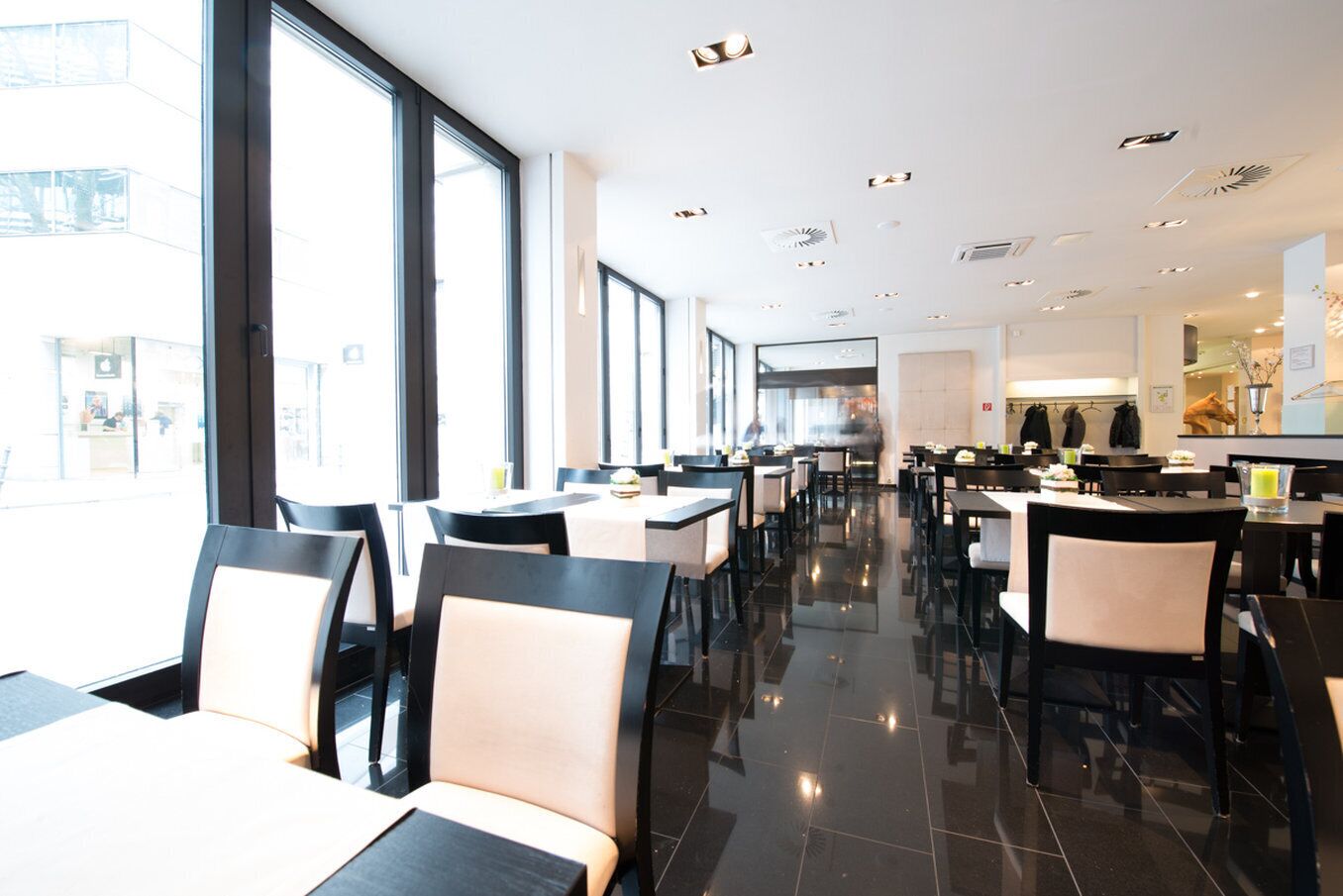 A modern restaurant with high ceilings, large windows, and a clean, polished floor.