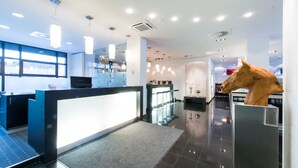 A modern reception area with a reception desk, bar stools, a large horse sculpture, and a large window with a city view. - Aquis Grana City Hotel (Aachen)