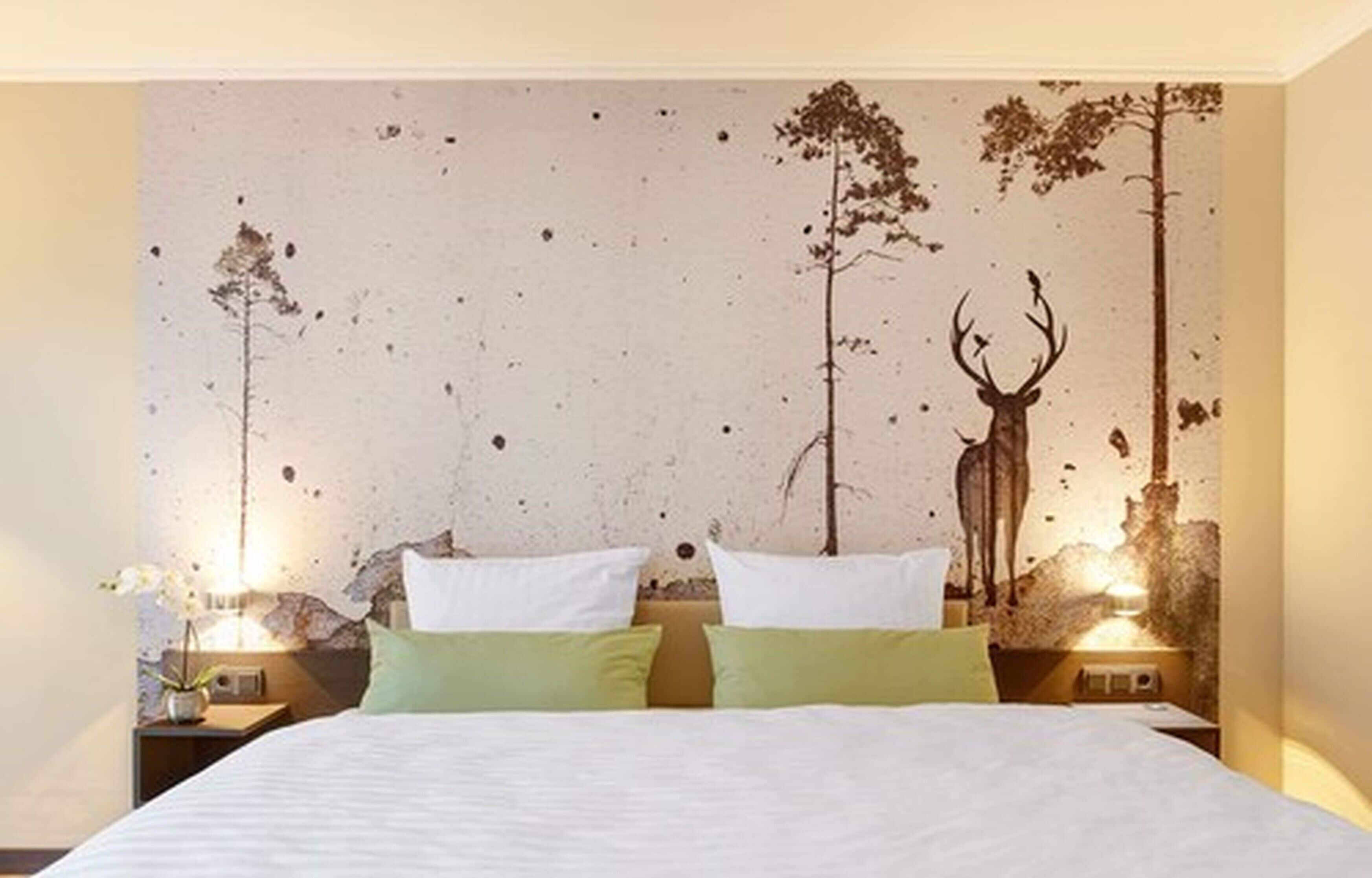 A bedroom with a bed, two nightstands, and a wall mural of a forest scene.