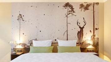 A bedroom with a bed, two nightstands, and a wall mural of a forest scene.