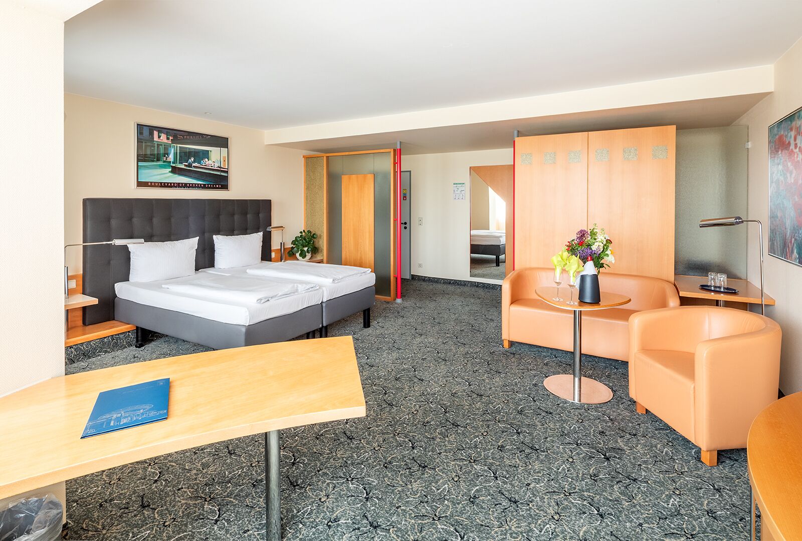 Habitación de hotel con cama, escritorio, silla, una pequeña mesa con un florero y armario.