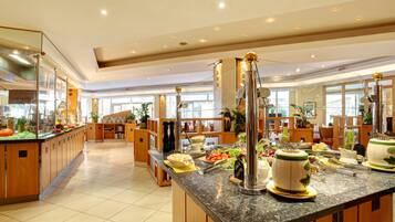 Eine großzügige Hotelhalle mit einem Marmor-Rezeptionsschalter, einem Frühstücksbereich mit verschiedenen Speisen und einem großen Fenster, das für natürliches Licht sorgt.