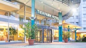 The exterior of the Tierpark Hotel with a glass facade, a curved entrance, and potted plants in front. - Abacus Tierpark Hotel Berlin (Berlin)
