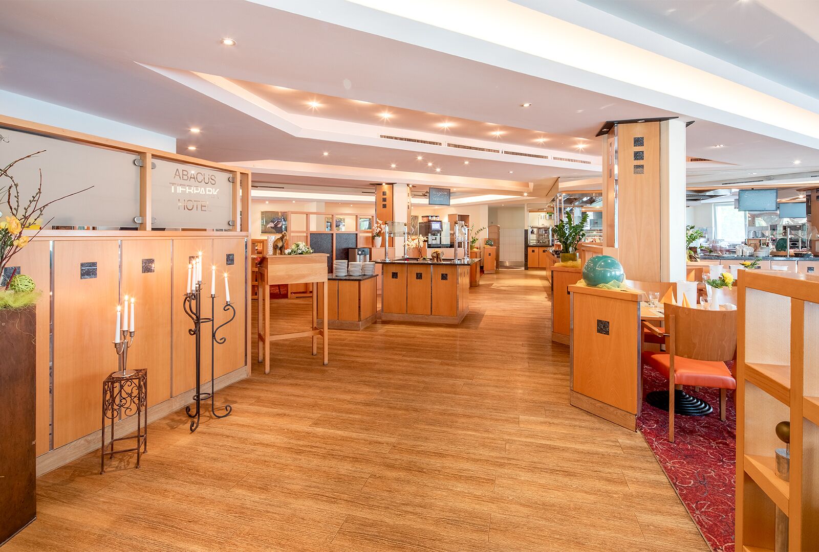 A hotel lobby with wooden flooring, a reception desk, and a seating area with a red carpet.