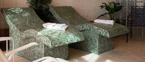 Två gröna loungestolar med kakelbeklädd sits, tillsammans med handdukar, en krukväxt och en kakelbeklädd vägg med en dekorativ list.