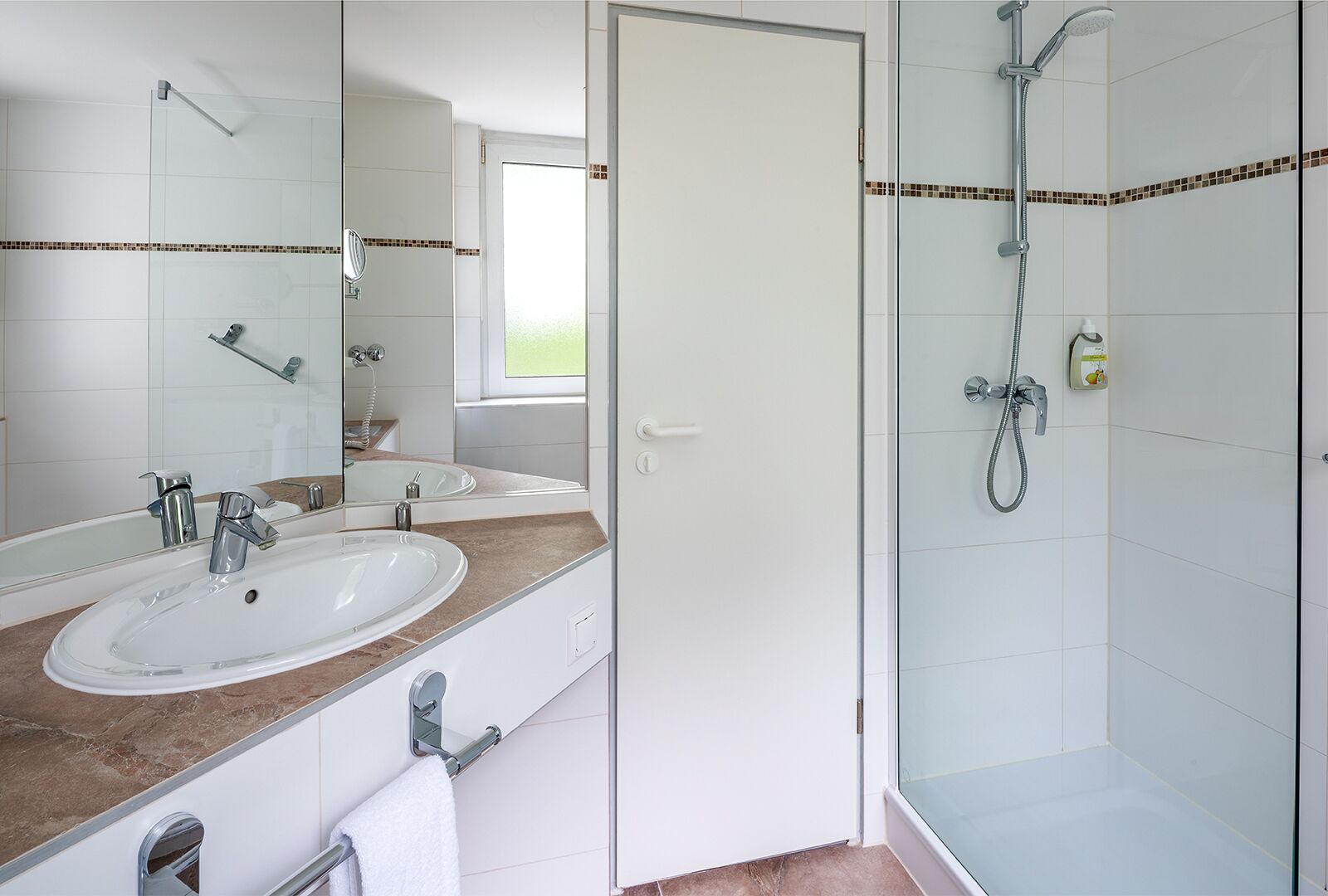 Un baño con lavamanos blanco, un espejo, ducha y toallero.