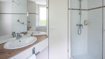 Un baño con lavamanos blanco, un espejo, ducha y toallero.